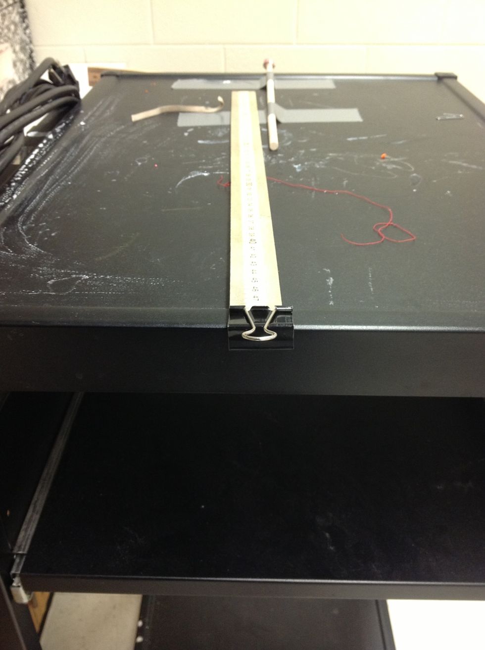 1.  Clip the binder clip to the end of a half meter stick.    2. Lay the stick on your desk so that only the clip extends over the edge.