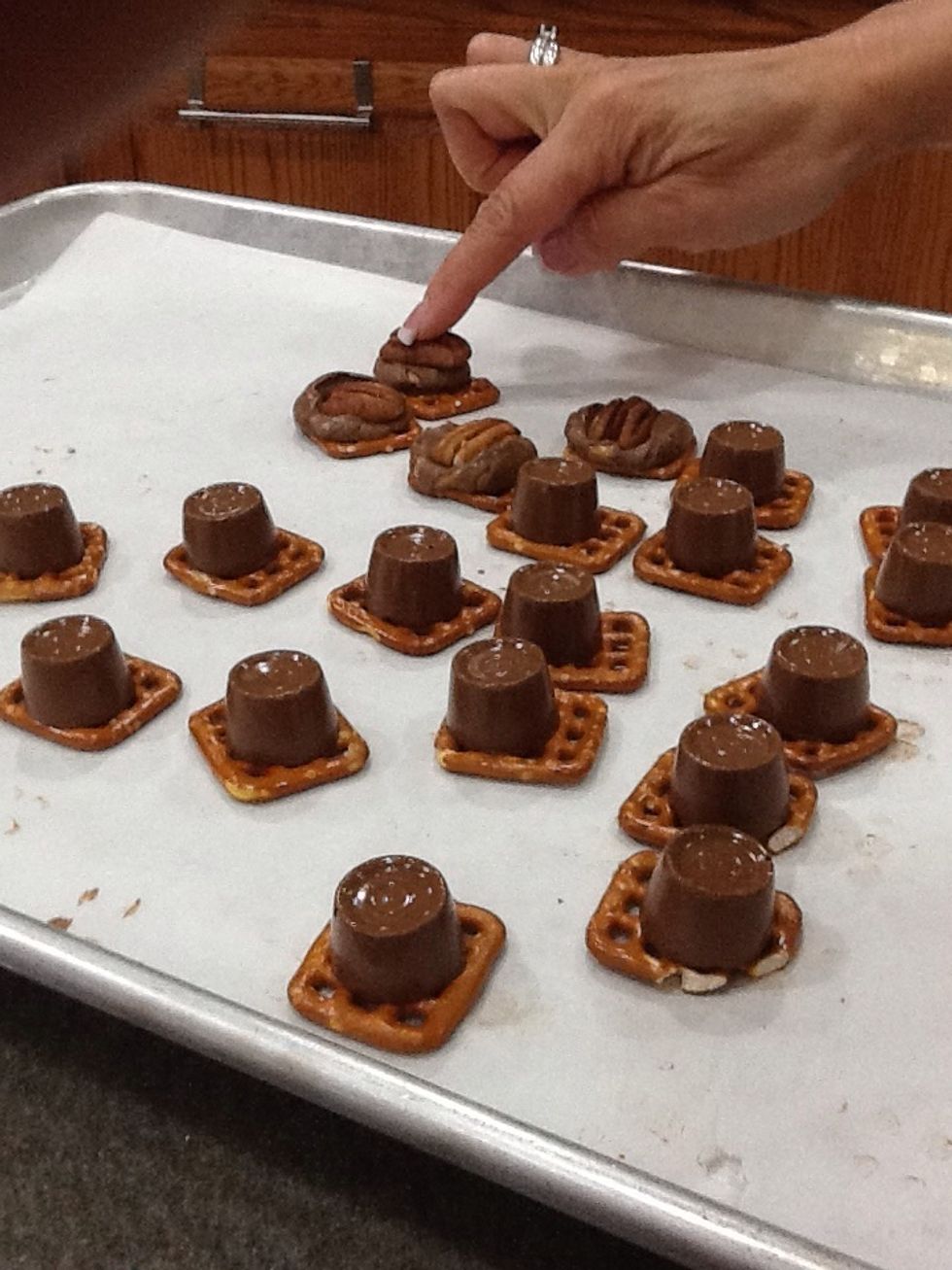 1) Remove pan from oven. 2) Place a pecan halve on top of each pretzel.  3) Push pecan down.  Work quickly, before the Rolo candy cools.