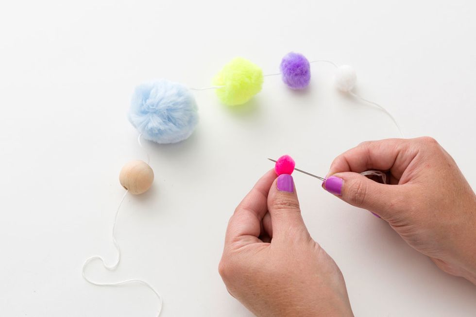 1. Thread a long piece of embroidery thread through your needle and then string on your wood bead and five pom poms, starting with the largest and ending with smallest.