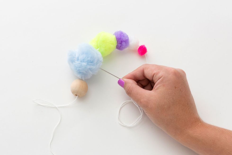 2. Slide all the pom poms next to each other and then pierce your needle back through the first, largest pom pom.