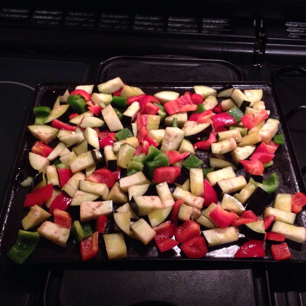 2. Usando un cuenco, a\u00f1adimos un poco de aceite a la berenjena y los pimientos. P\u00f3ngalos sobre una bandeja del horno y \u00e1selos en el alto del horno por 20 min., o hasta lo que est\u00e9n tostados los bordes