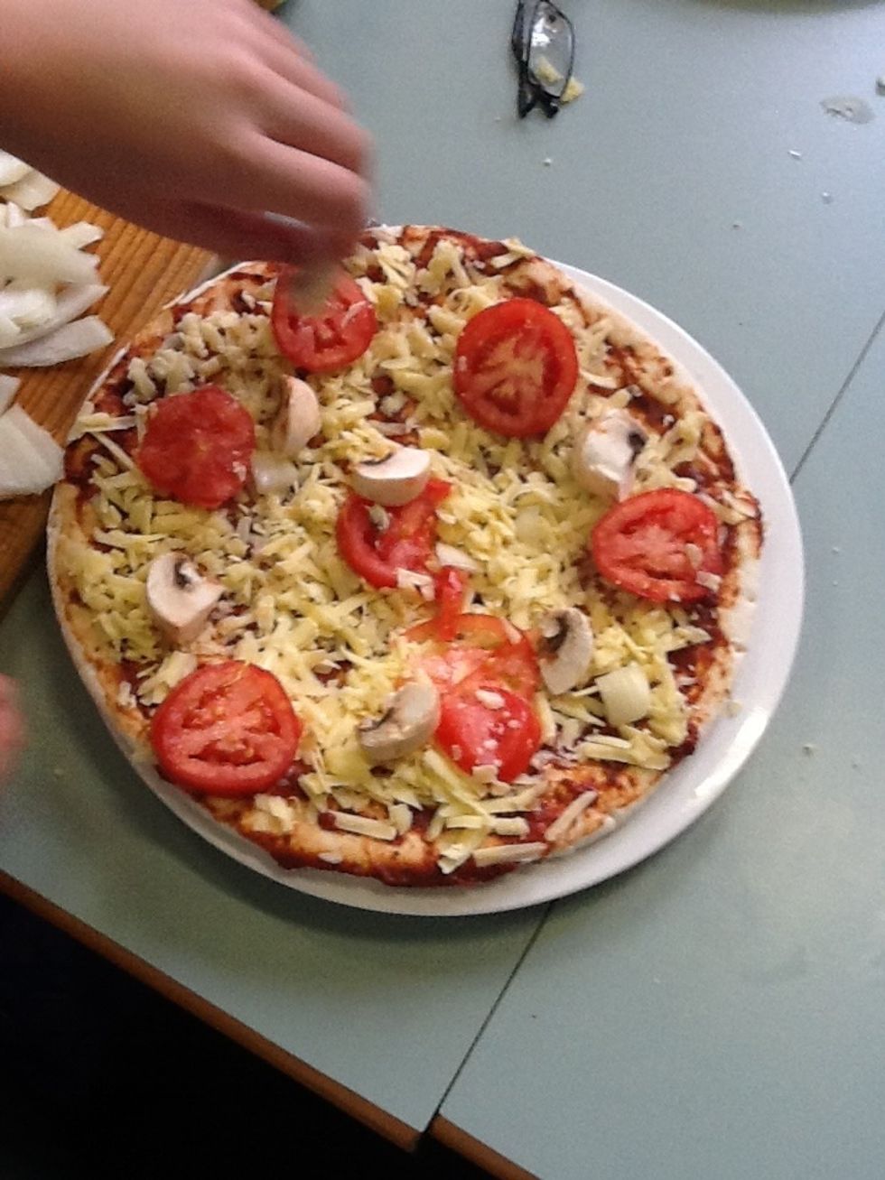 (9)Sprinkle the mushrooms , the Onion , Tomatoes and the salami on the pizza base.