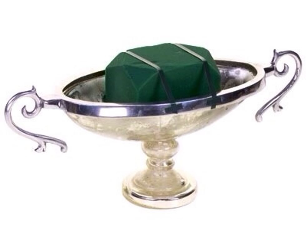 A silver mercury glass footed container elevates the design with a glamorous feel. Secure a soaked piece of floral foam into the container using wet tape in a railroad tracks pattern .