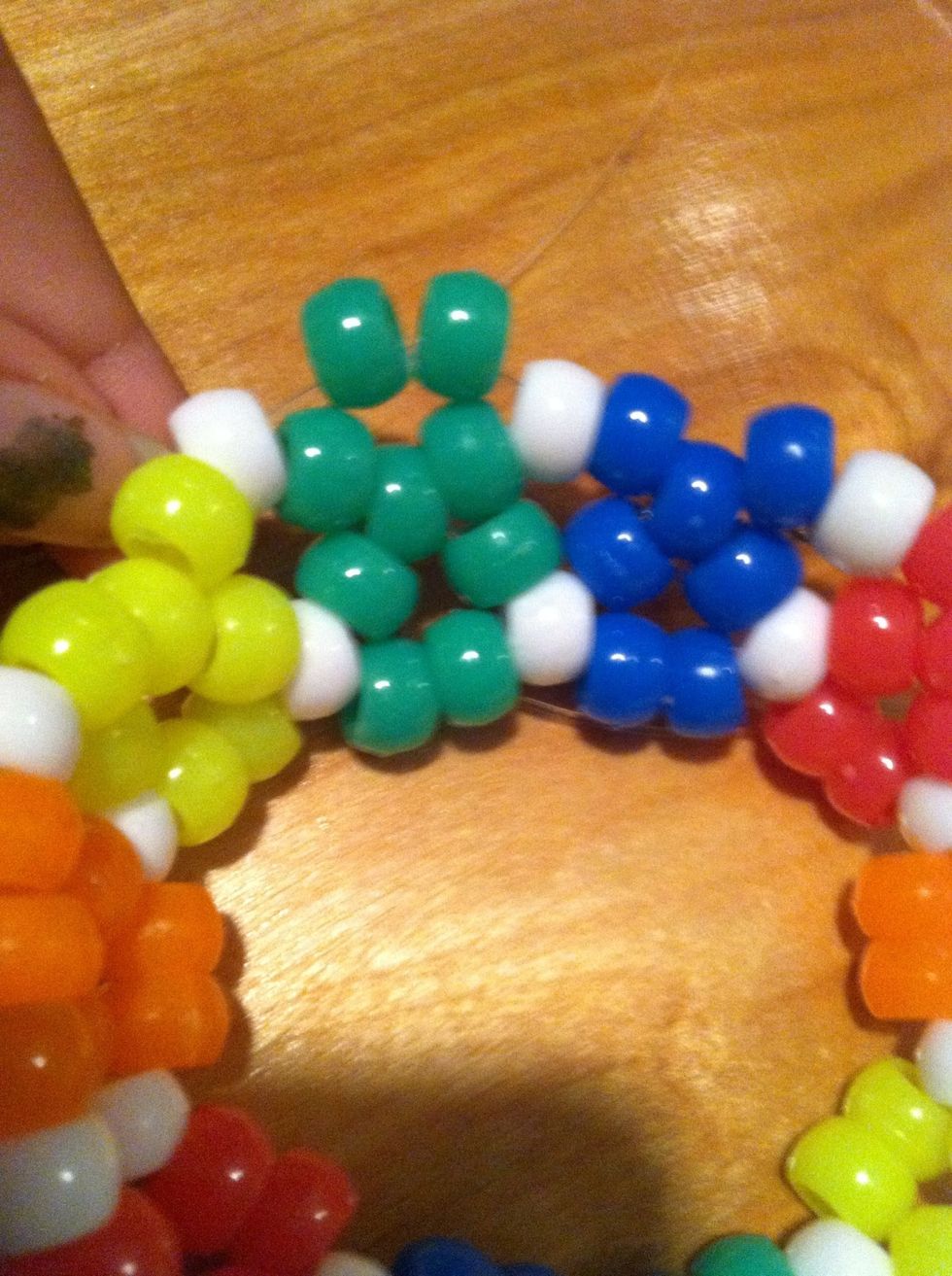 Add 2 green beads to your string and thread it through the next white bead sticking up.