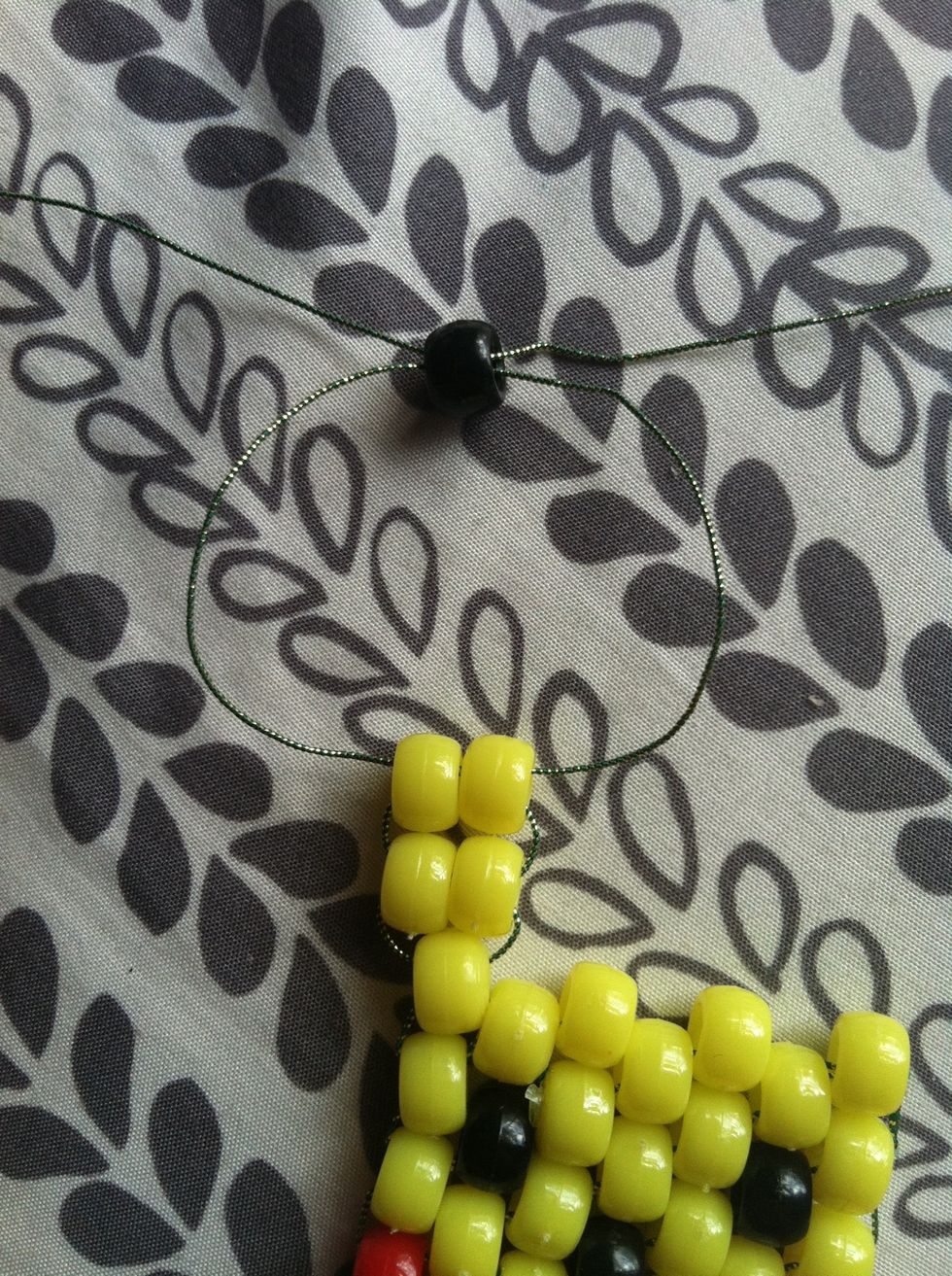 Add 2 more yellow beads, then once you tighten those add a black bead. Tie the strings into a knot and repeat to the other side.