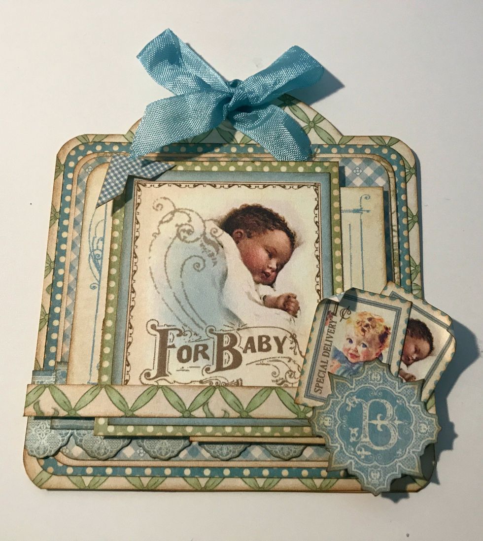 Add a blue checkered photo corner sticker on the top left hand side of the baby image. To finish the top of the tag, add a light blue ribbon bow.