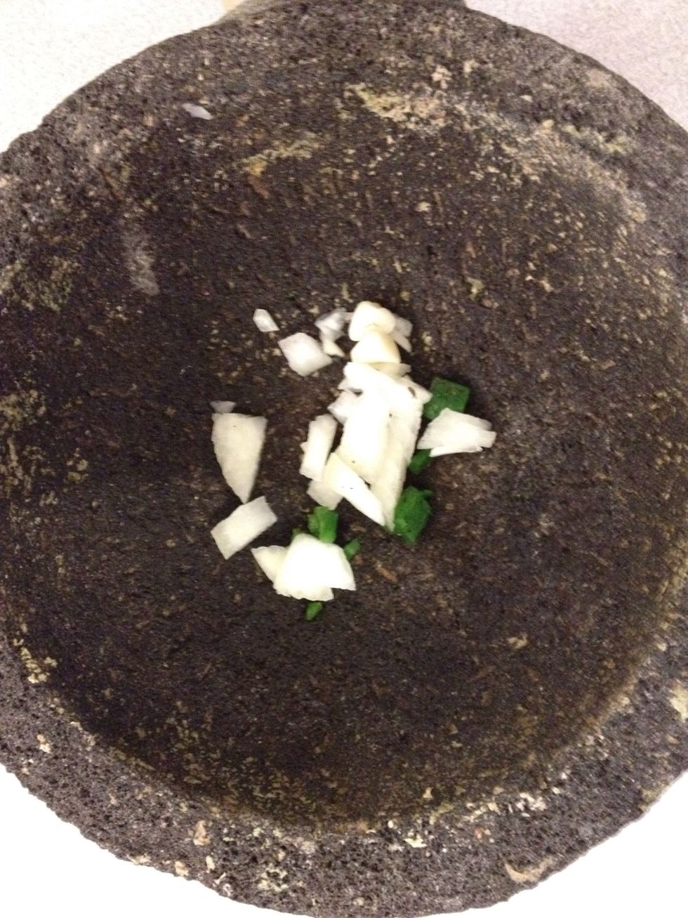 Add a few pieces of diced jalape\u00f1o, a few leaves of cilantro, and some onion to the molcajete.
