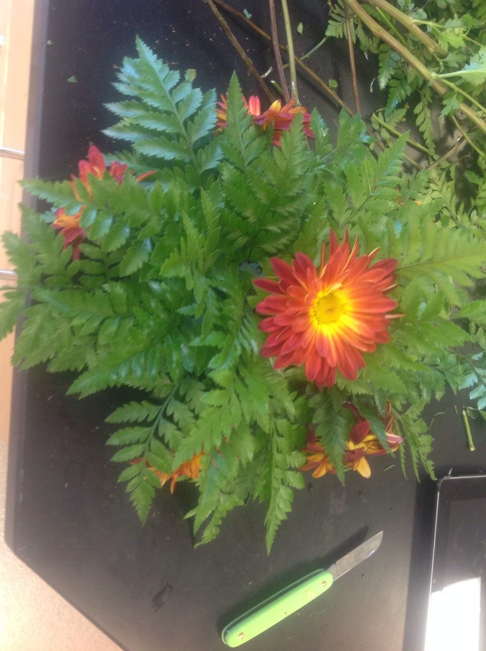 Add a flower at the center of your arrangement, no higher than your leather leaf. Add five other flowers around the bottom of the oasis as well.