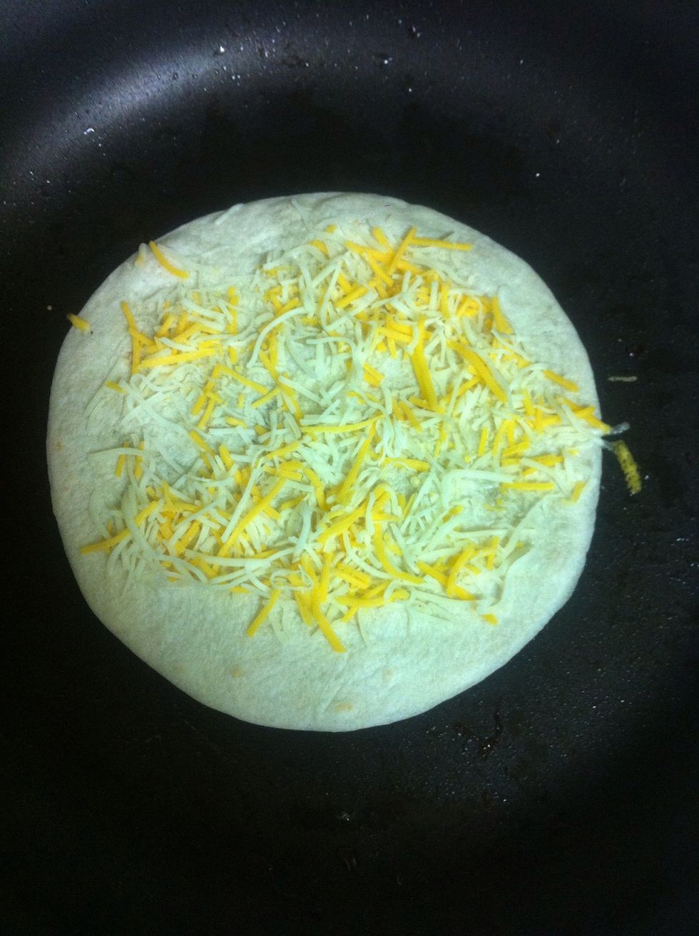 Add a tortilla to the pan and put cheese on top