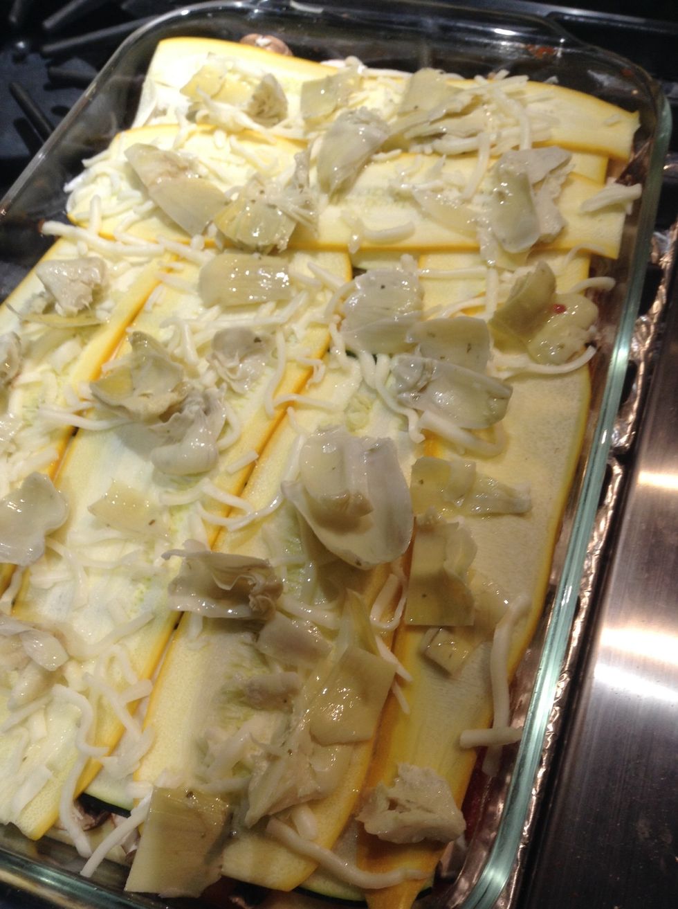 Add another layer of pasta and sauce, followed by mushrooms, ricotta, 2 layers of zucchini, mozzarella, and artichoke hearts.