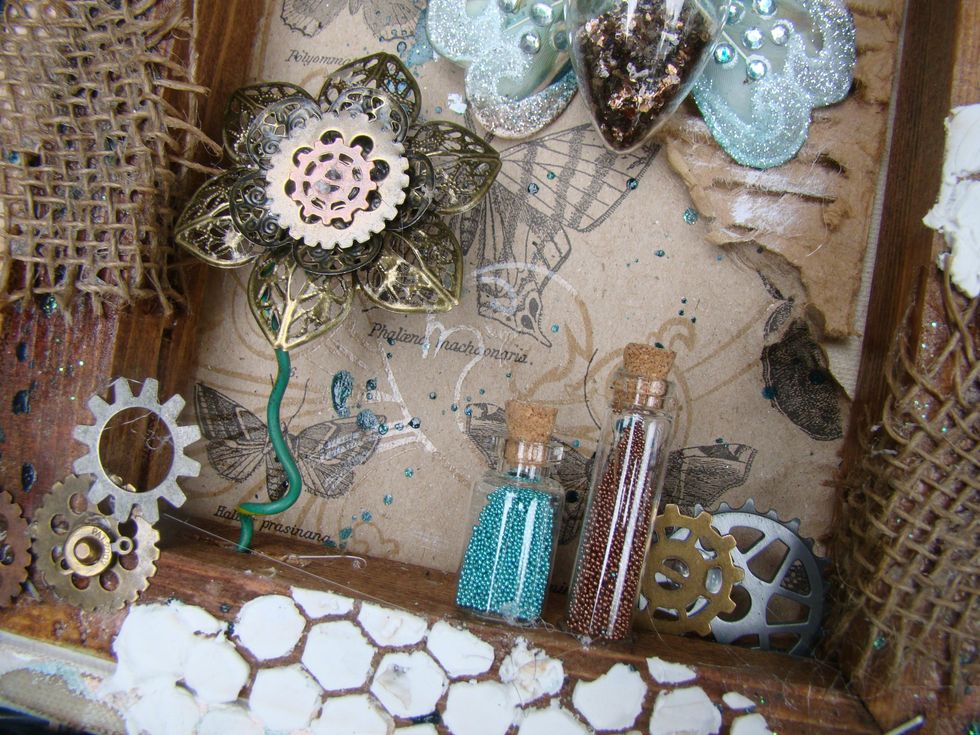 Add different size bottles and fill with seed beads, glue to canvas frame. Tuck more gears and cogs in the corners and edges of your canvas.