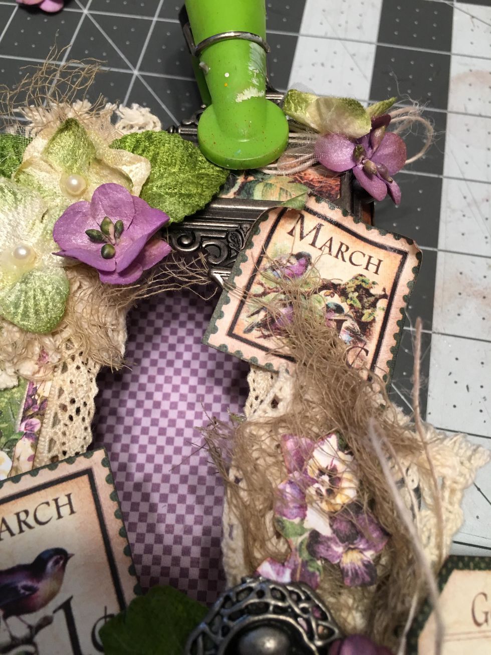 Add flowers and a button string bow to the right top of the label holder to hide the brad hole & a purple flower to the left. Clip & hold the metal piece in place until it dries completely. Glue