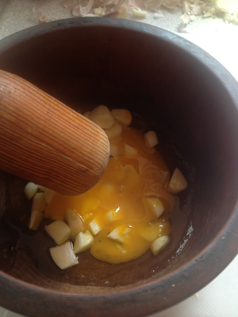 Add garlic to mortar along with one and a half table spoons of olive oil, about half a tea spoon of salt and one egg yolk. Start grinding vigorously.