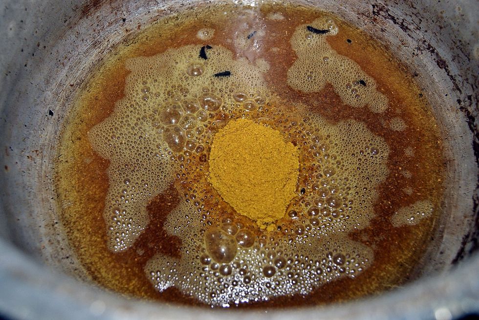 Add it to the hot oil. Make sure all the powder dissolves into the oil and fries up well. Curry that isn't cooked well can cause a serious problem in the belly if yuh know what ah mean.