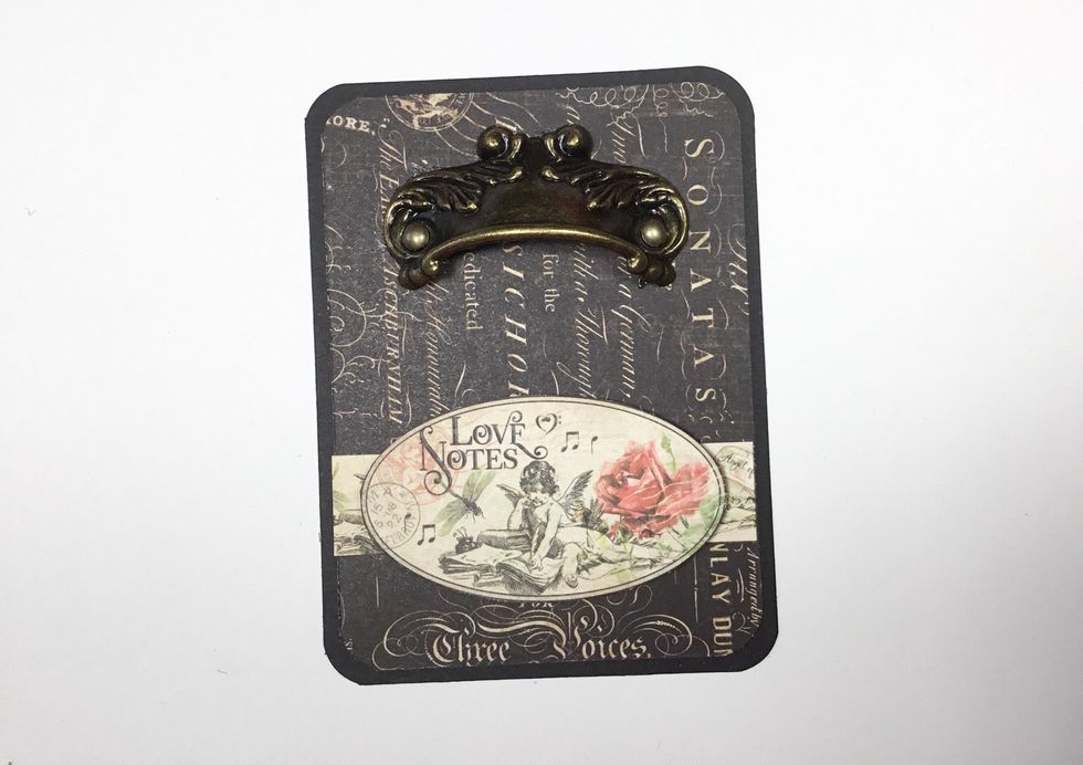 Add matching pattern paper and a G45 metal door pull to the remaining piece of cardboard. This will become like the false bottom on the bottom of the box to allow for things to be stored underneath.