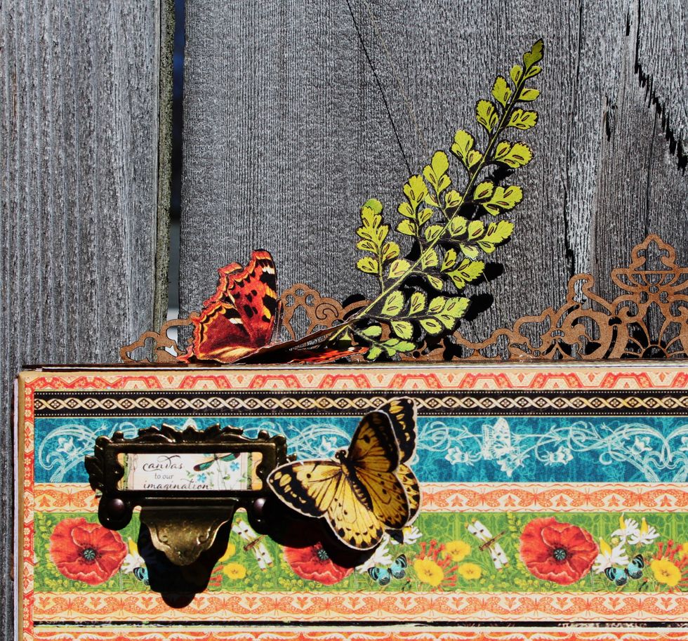 Add natural chipboard to top of frame with fussy cut leaves and butterflies to top of frame. Adhere metal label holder to top of sentiment; adhere to top of frame along with butterfly.