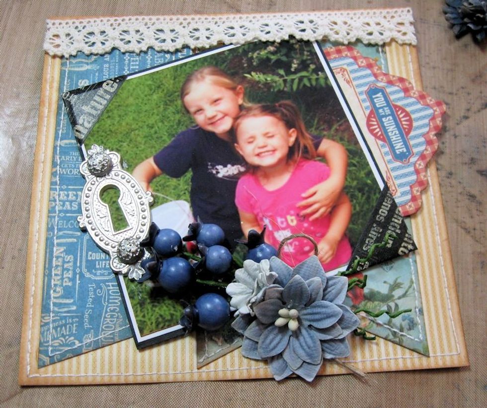 Add Ornate Keyhole with brads on left hand side of photo, as seen here. Then use hot glue to add blueberry picks, followed by flowers.