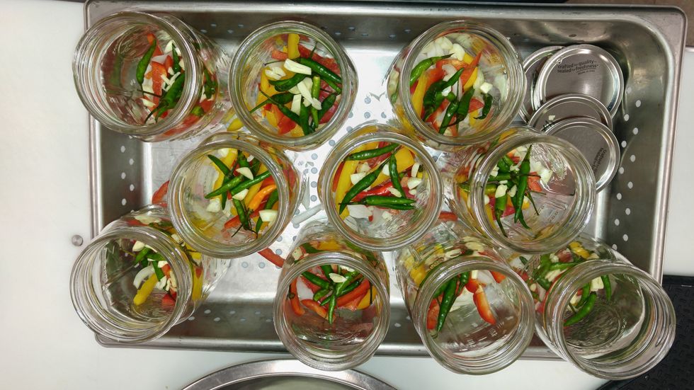 Add peppers, onions, garlic and hot peppers to the jars.