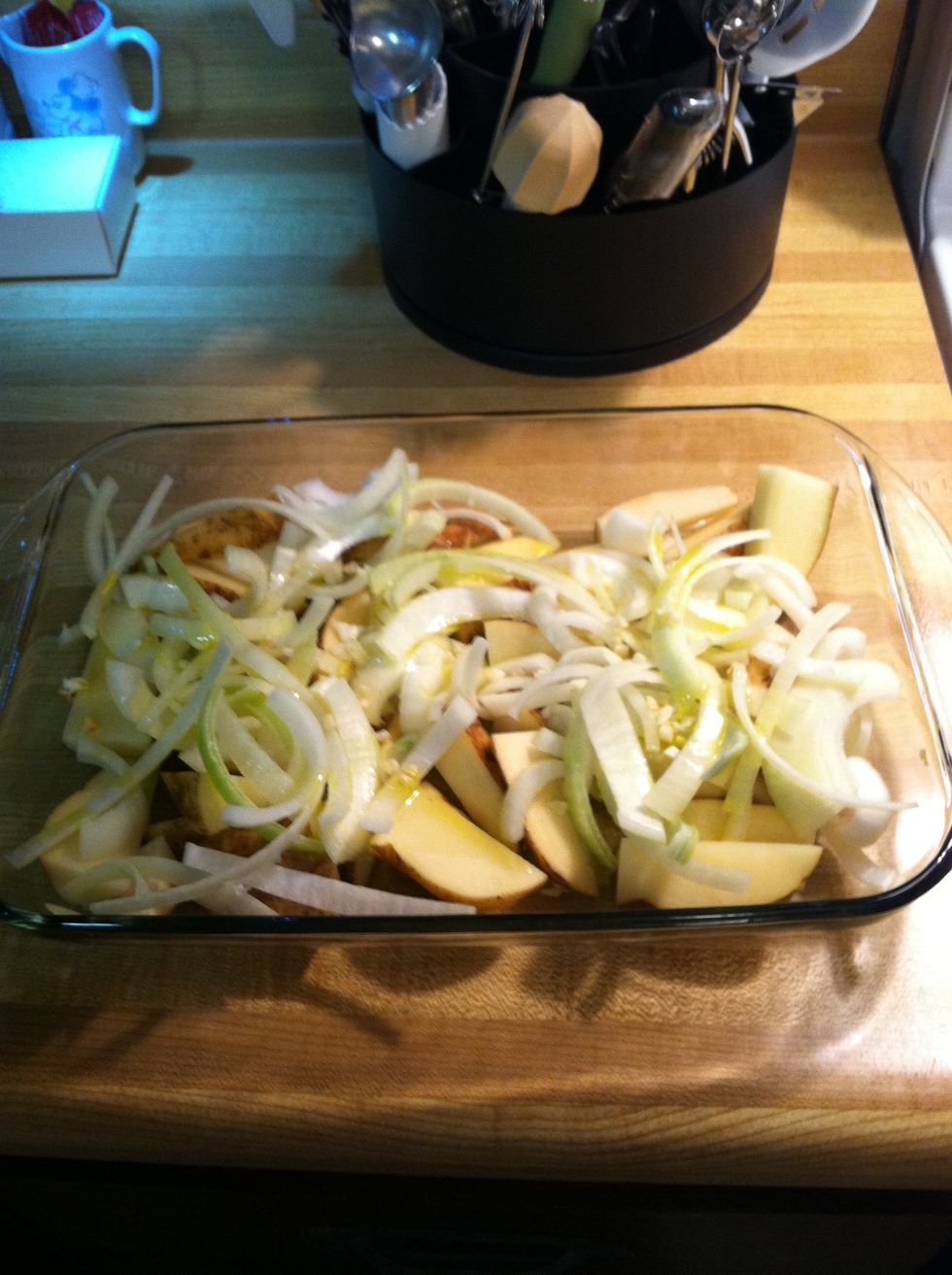 Add potato wedges , onion slices and garlic to your baking dish and drizzle with olive oil.