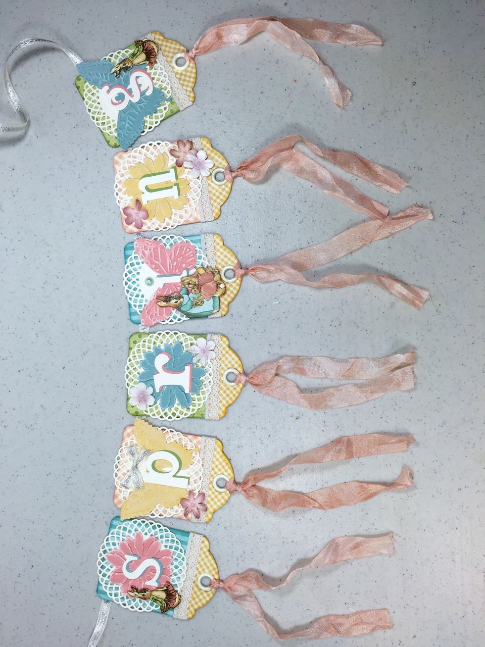 Add pretty ribbon to the bottoms of each banner tag. I colored ivory seam binding ribbon with Tattered Rose Distress Stain spray.