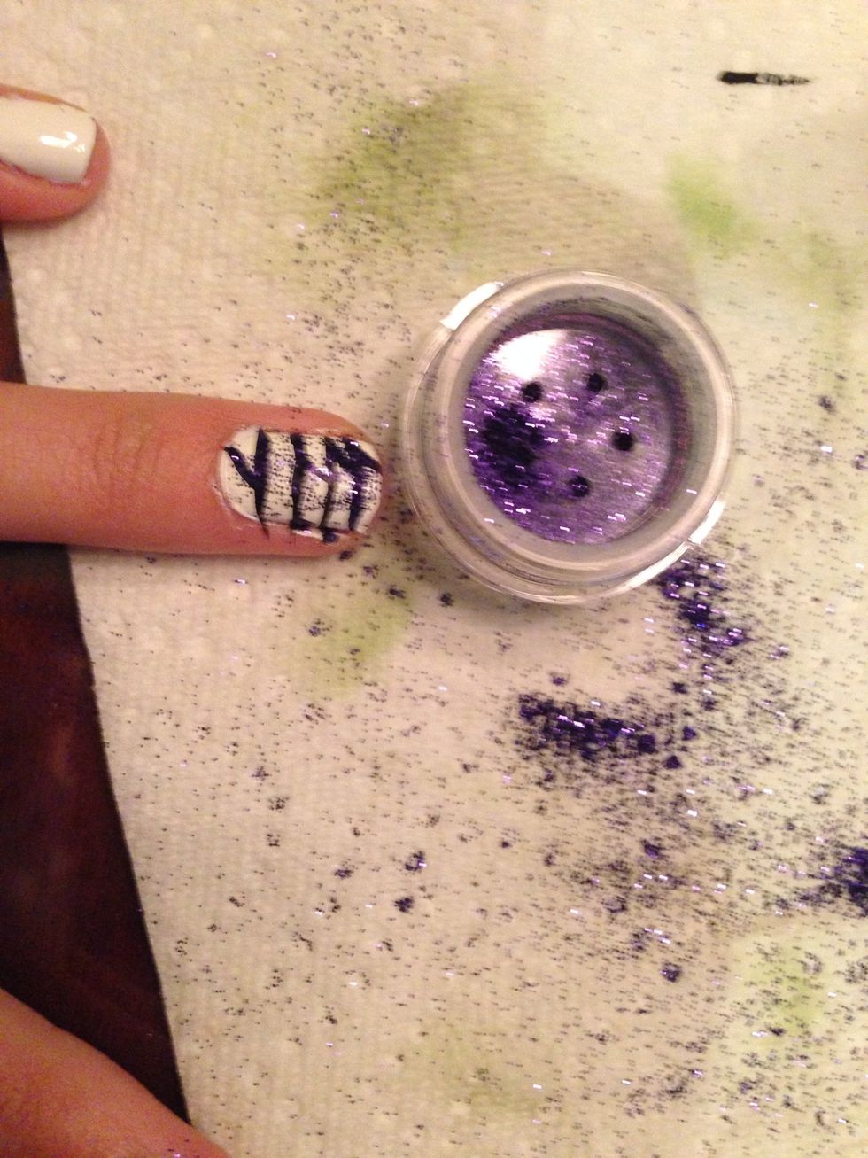 Add purple glitter to the nail and blow off the extra