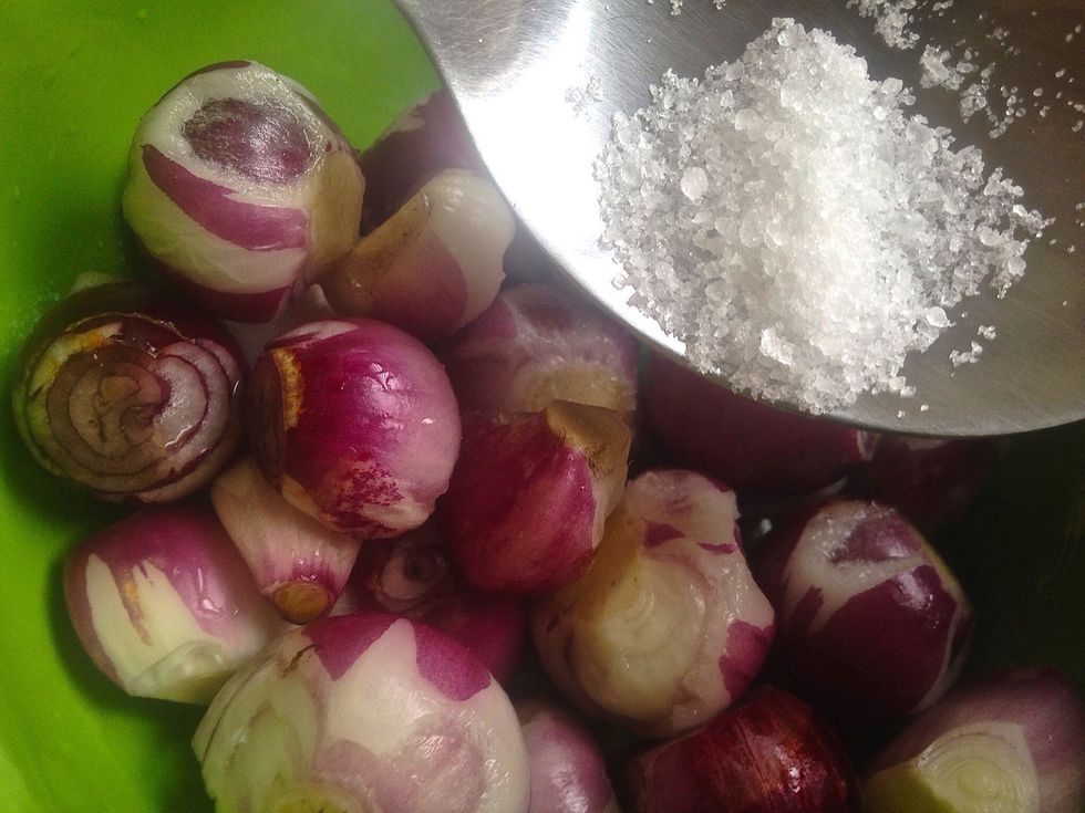 Add salt into a container of water. Then add the peeled shallots.