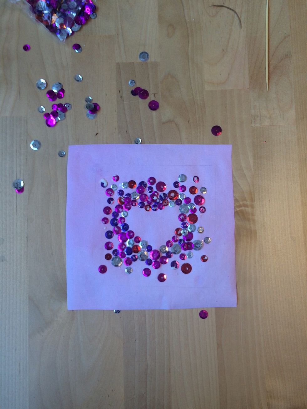 Add sequins around the outside of the heart, making them less dense toward the edge of the paper.