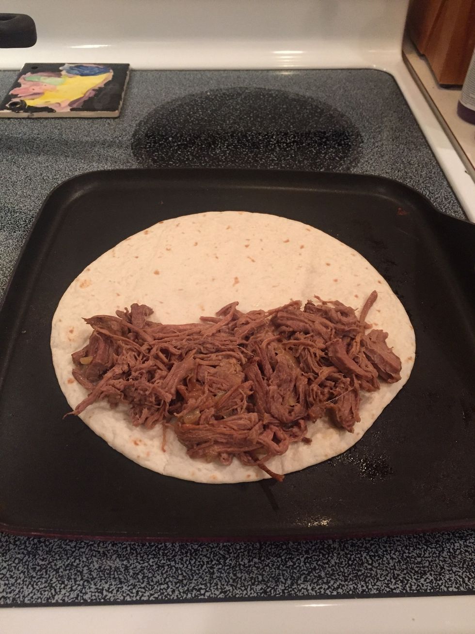 Add shredded beef on one side of the tortilla.