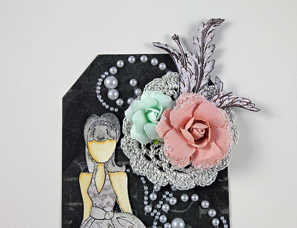 Add smaller doily to the top, right side of the tag. Add flowers and flourishes cut from "Galerie d' Orleans" patterned paper.