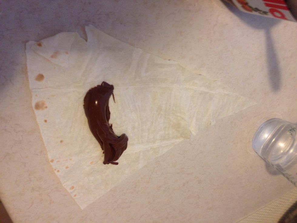 Add some of the Nutella to the lower centre . Leave space to fold and roll. Stick the edges with some water. You can add some chopped hazelnuts here before rolling!