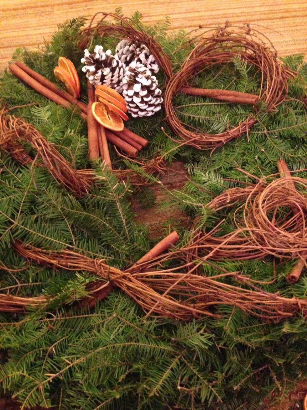 Add the cinnamon sticks to the wreath. We are trying to make a bit of a corsage up by the pinecones. Next, wire in the dried oranges.