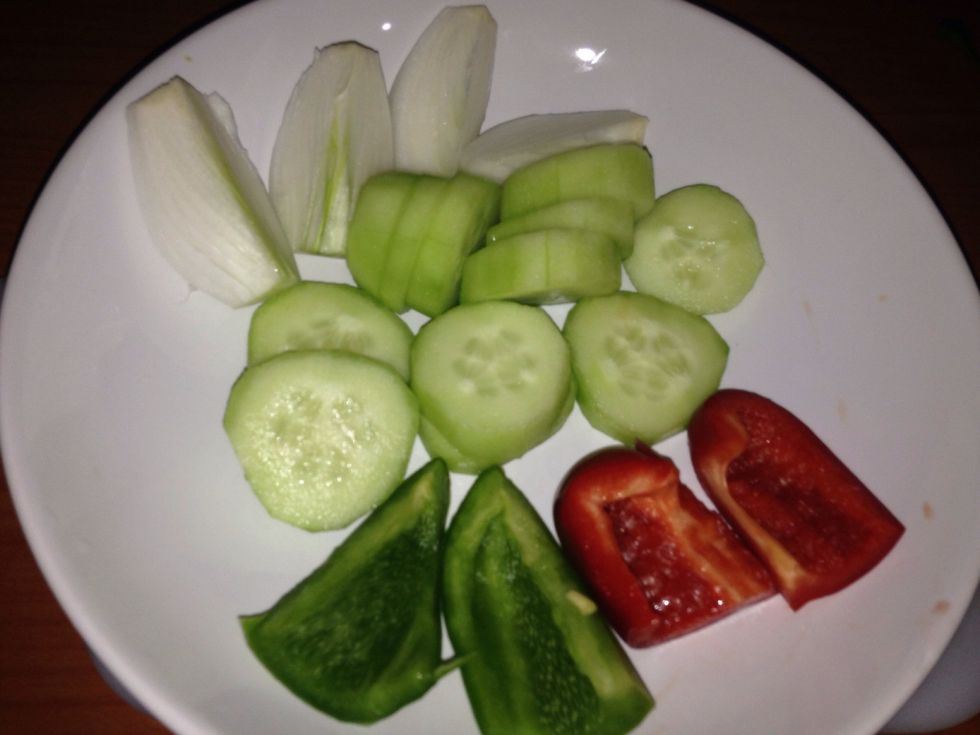 Add the cucumber, 2 pieces of red pepper, 2 pieces of green pepper and onion (a\u00f1adir el pepino, 2 trozos de cada pimiento y la cebolleta)