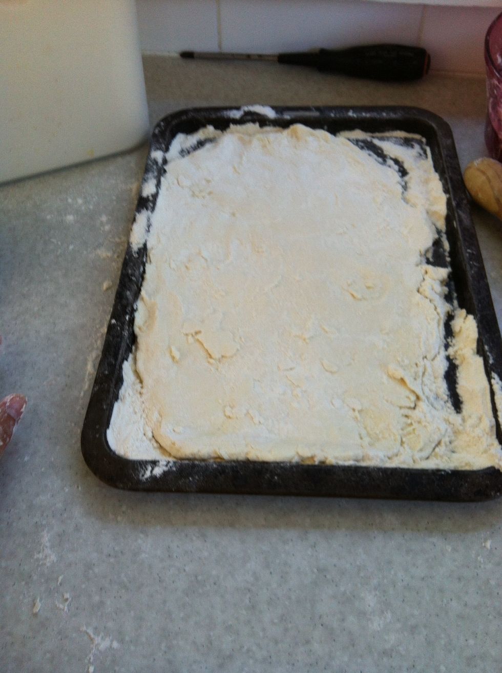 Add the pizza dough and with a rolling pin, roll out the dough.