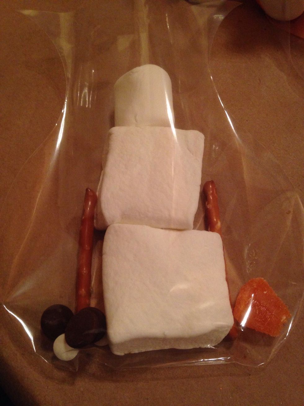 Add to bag: -2 large, 1 medium, & 2 small marshmallows. -3 chocolate chips, 1 orange candy slice, 2 candy eyes, 2 pretzel sticks.