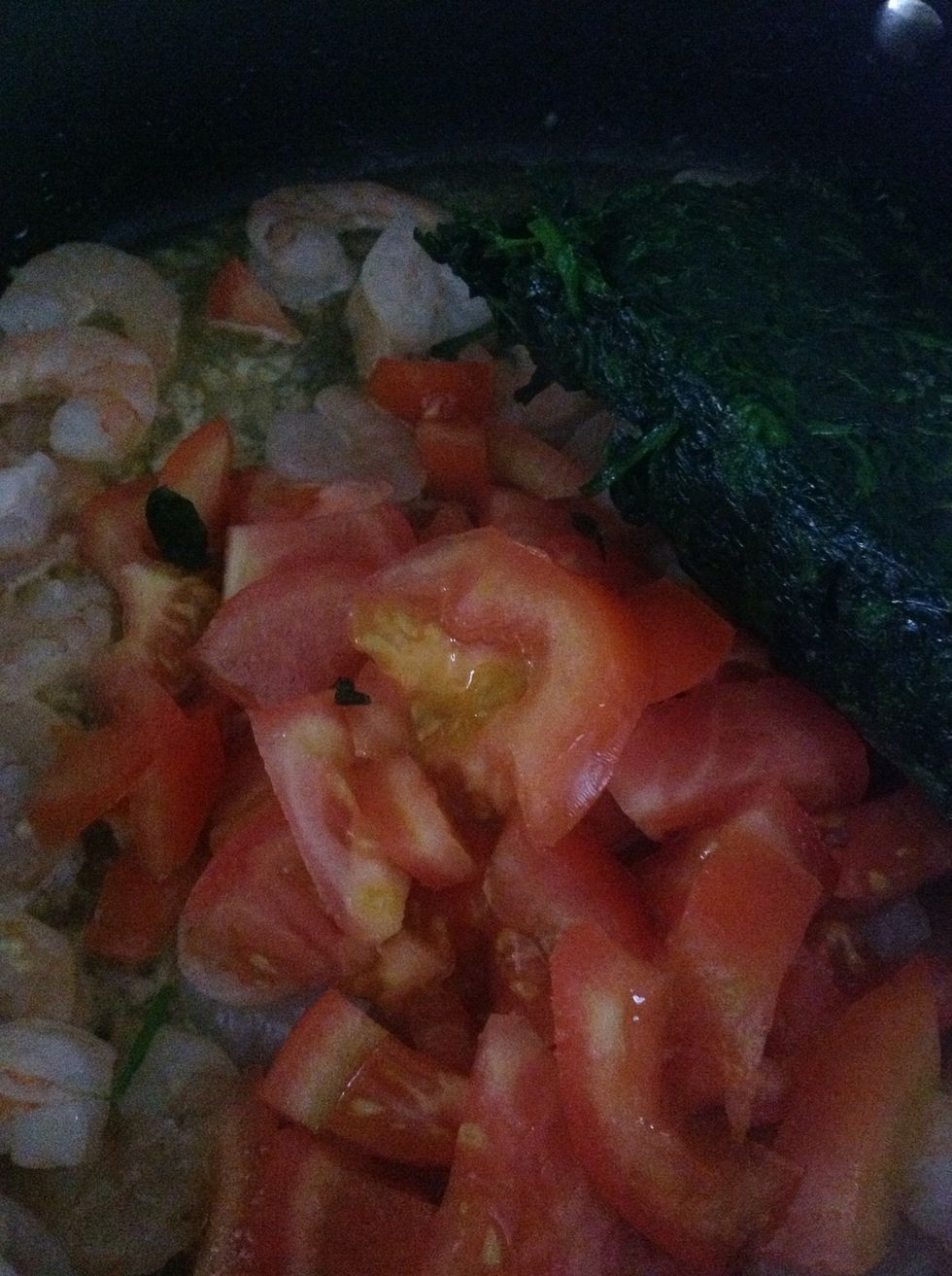 Add tomato and partially thawed spinach to cooked shrimp, heat until warm, and the spinach is thawed and mixed well together.