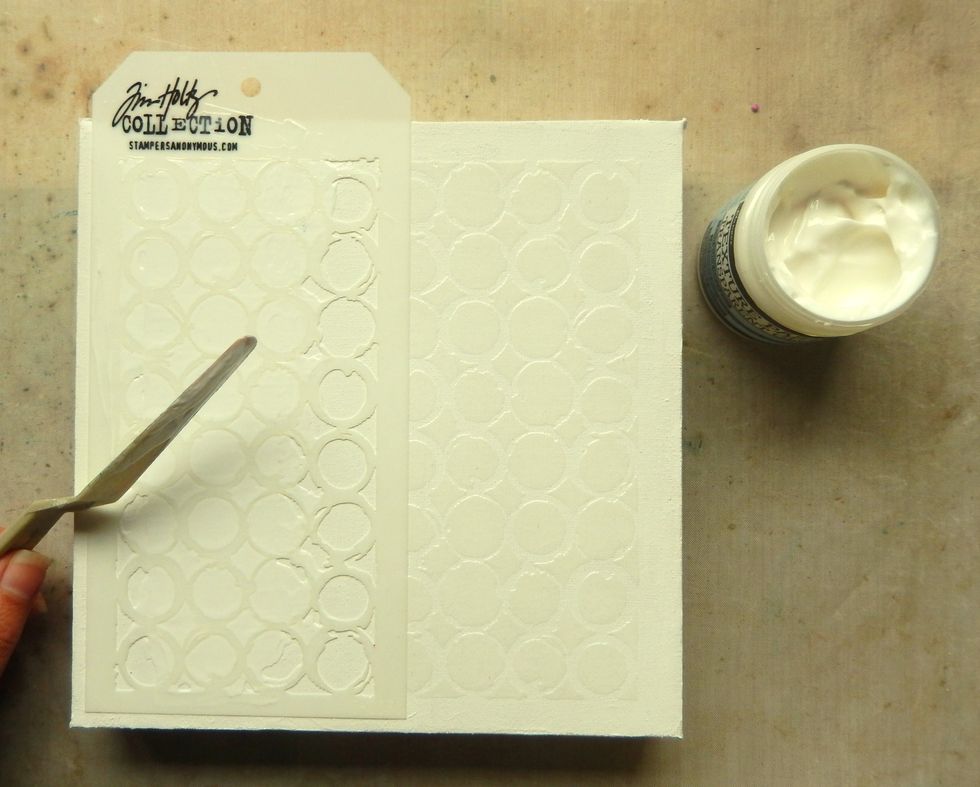 Add Transparent Gloss Texture Paste through the Ringer Layering Stencil across the middle of the canvas, leaving a border un-stencilled. Allow the paste to dry.