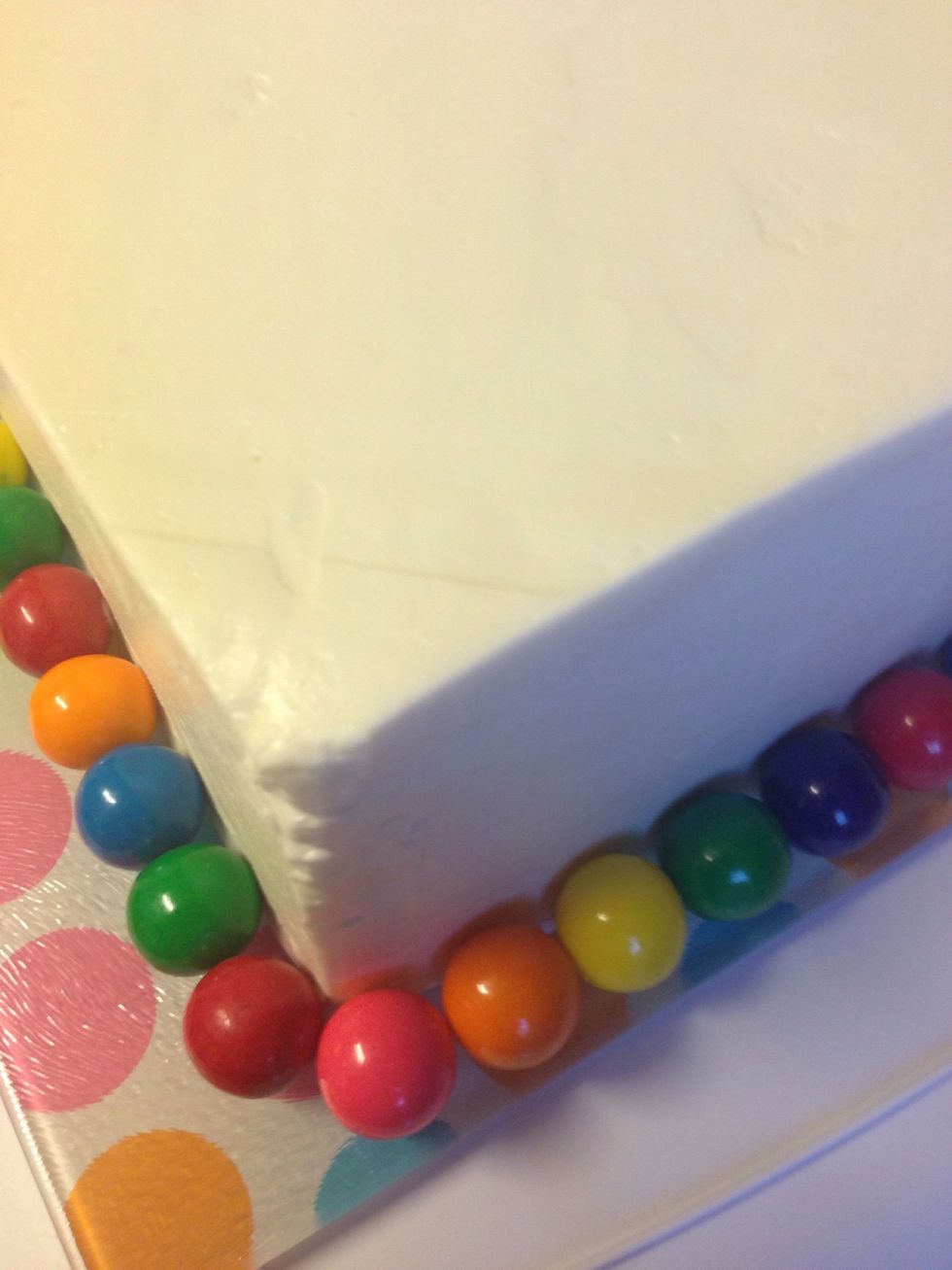 Add your gum balls around the base of the cake. Press gently to adhere them to the frosting.
