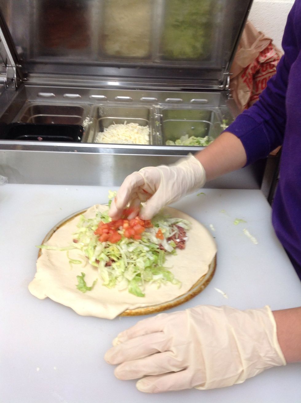 Adding tomatoes to lettuce and bacon on the calzone
