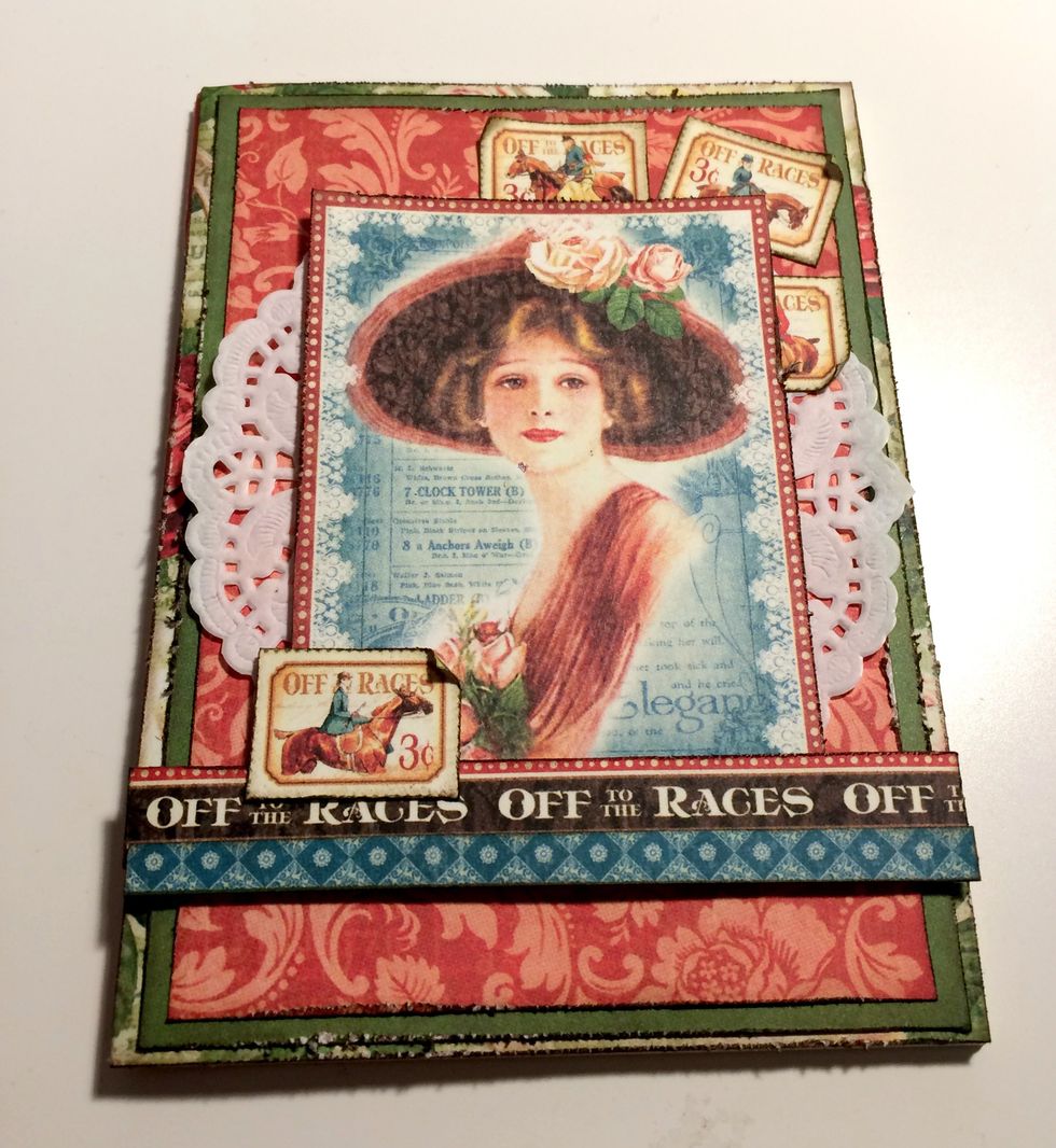 Adhere 3 stamps in the top right corner underneath the lady. Roll the corner down or up on each stamp. Adhere 1 stamp in the bottom right corner overtop of the lady. Roll the top corner down.