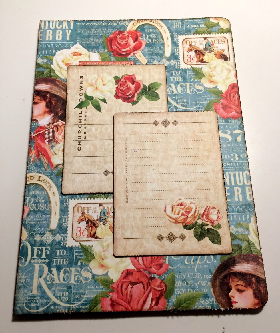 Adhere blue/rose paper to the front of the notebook. Adhere the 1 rose card 1" from the left and 1 3/4" from the top of the notebook. Adhere a 2 rose card 1 1/4" from the top and 5/8" from the right.