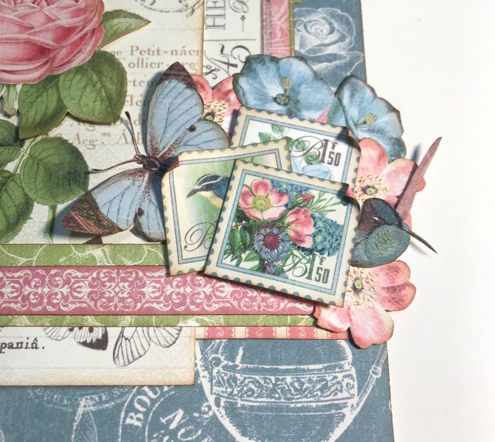 Adhere hummingbird overtop of 2 pink flowers. Adhere butterfly to left of pink flower. Foam square 1 stamp & adhere the other 2 stamps overtop of the empty space. On all 3 stamps roll down 1 corner.