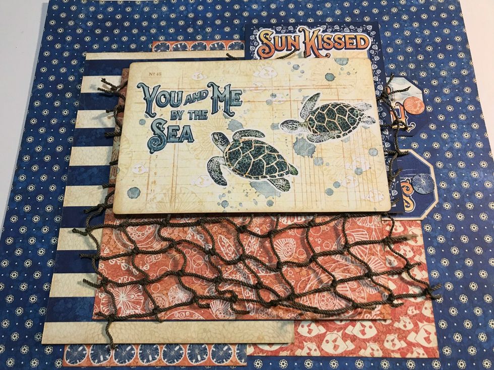 Adhere netting to the middle of the layered patterned paper. Foam square an ephemera card 2 1/4" from the top & 2 1/2" from the right of the paper.