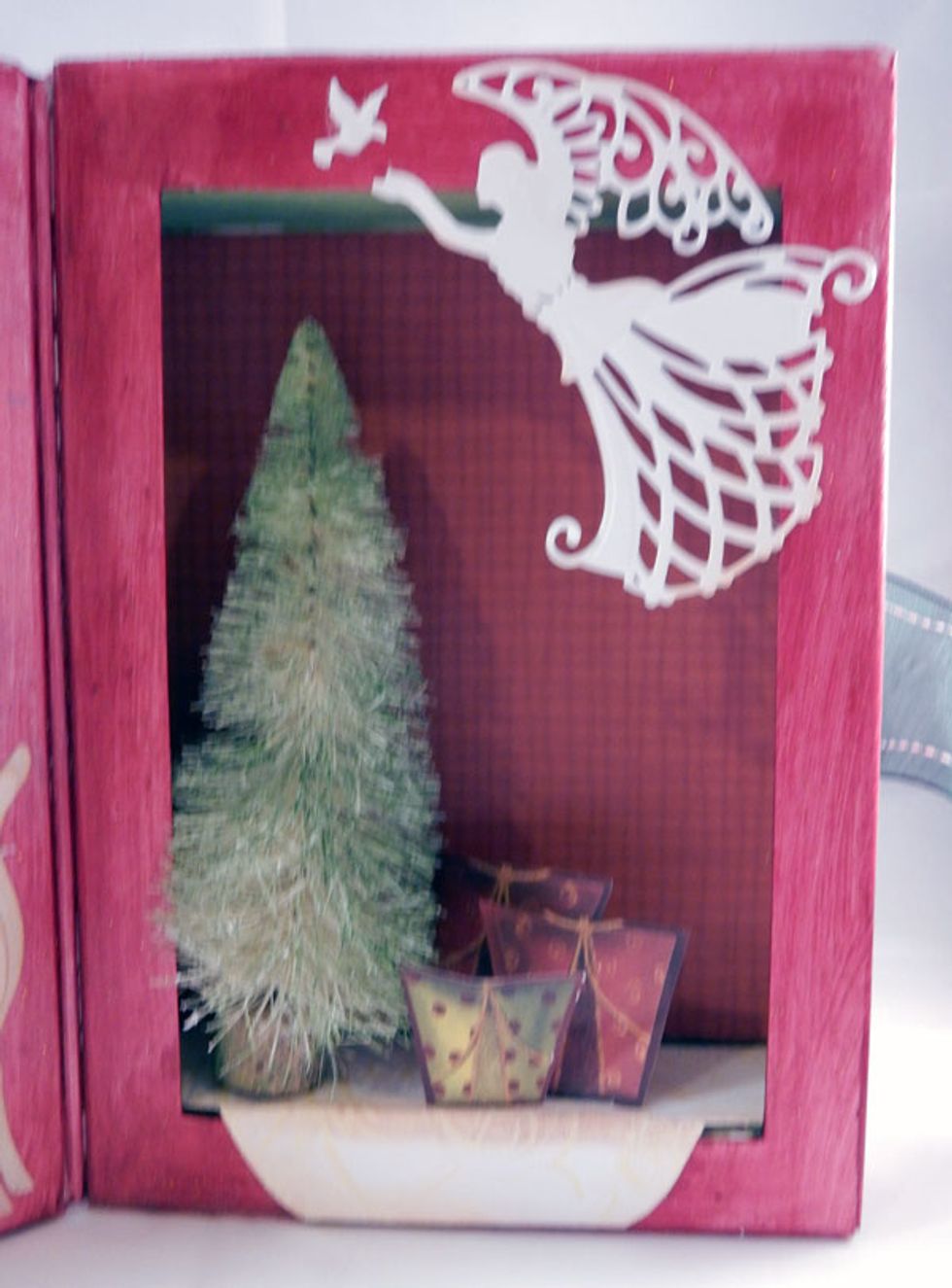Adhere pattern paper to the back and create a "skirt" for the tree.  Die cut an angel for the top of the book.  Adhere the tree and fussy cut packages to the bottom.