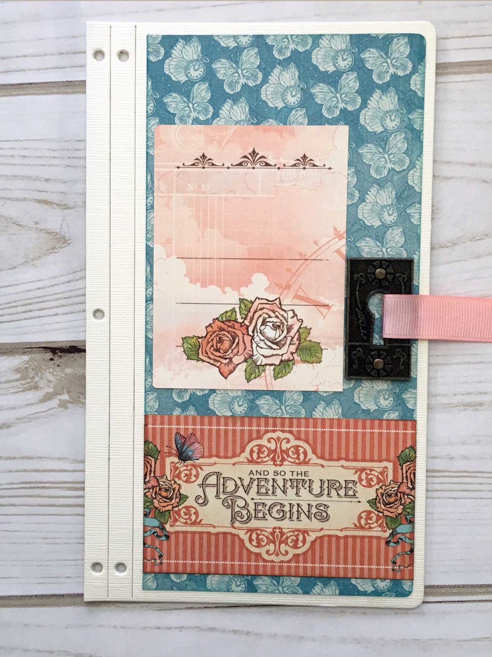 Adhere the back side of a small ephemera card to the left side, about 1 1/2" from the top.  Adhere the Adventure Begins card to the bottom as shown.