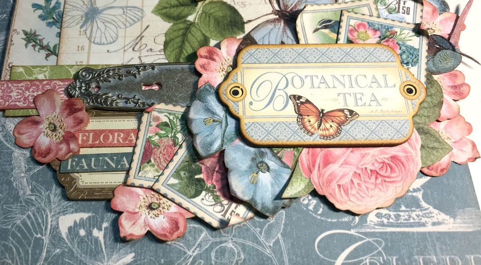 Adhere the Botanical Tea Chipboard piece overtop of parts of the flowers and stamps.
