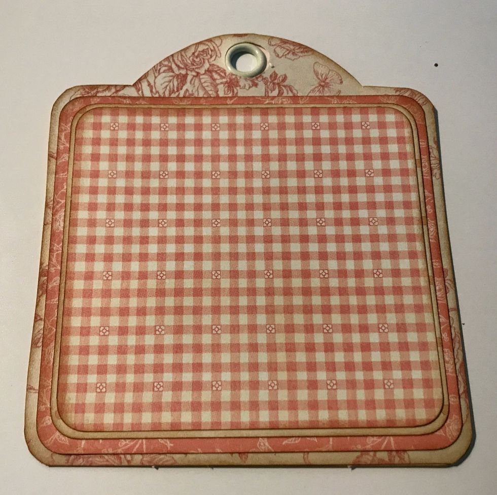 Adhere the pink/cream floral paper to the pink floral tag. Adhere the polka dot paper to the pink/cream floral paper. Adhere the pink checkered paper to the polka dot paper.