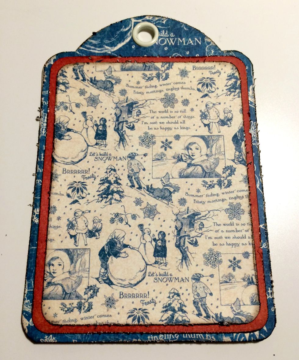 Adhere the red paper to the blue patterned paper tag. Adhere the cream and blue patterned paper to the red paper.