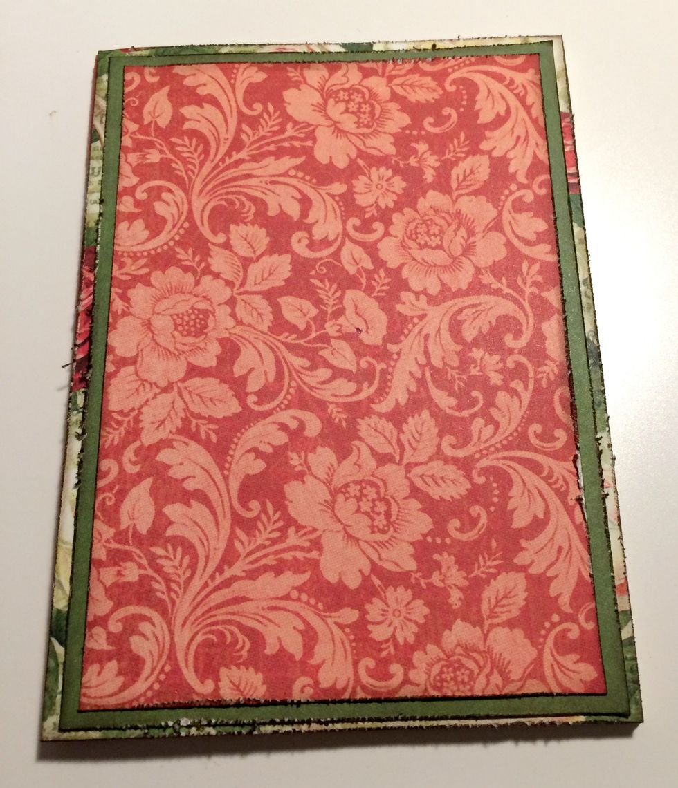 Adhere the rose paper to the front of the notebook. Adhere the dark green paper to the rose paper. Adhere the red damask paper to the dark green paper.
