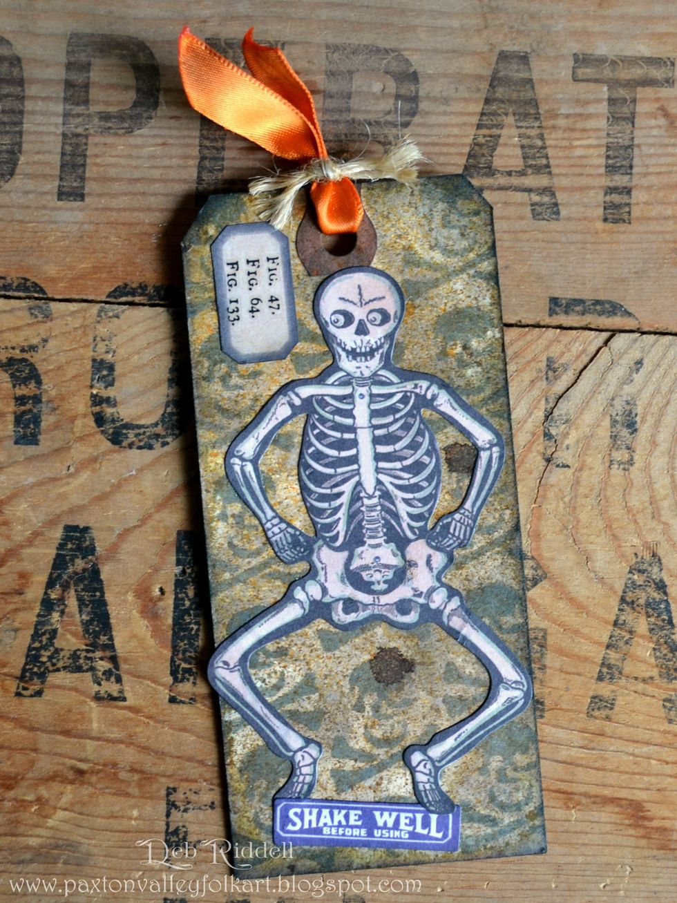 Adhere the skeleton from the Frightful Ephemera pack onto the trimmed Crossbones stenciled tag. Add Curiosities remnant rubs to a small tag from the Ephemera pack along with the 'shake well' label.
