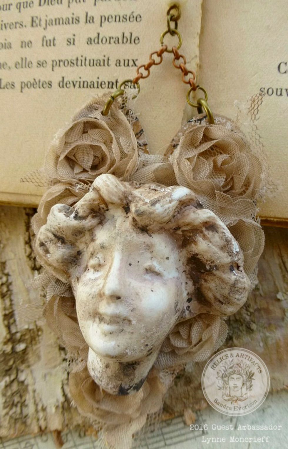 Adhere the stained lace rose trim to the large heart with Gel Medium. Let Dry. Glue the Facia Familiaris with E6000. Attach the heart to jewelry findings, chain and pearls.